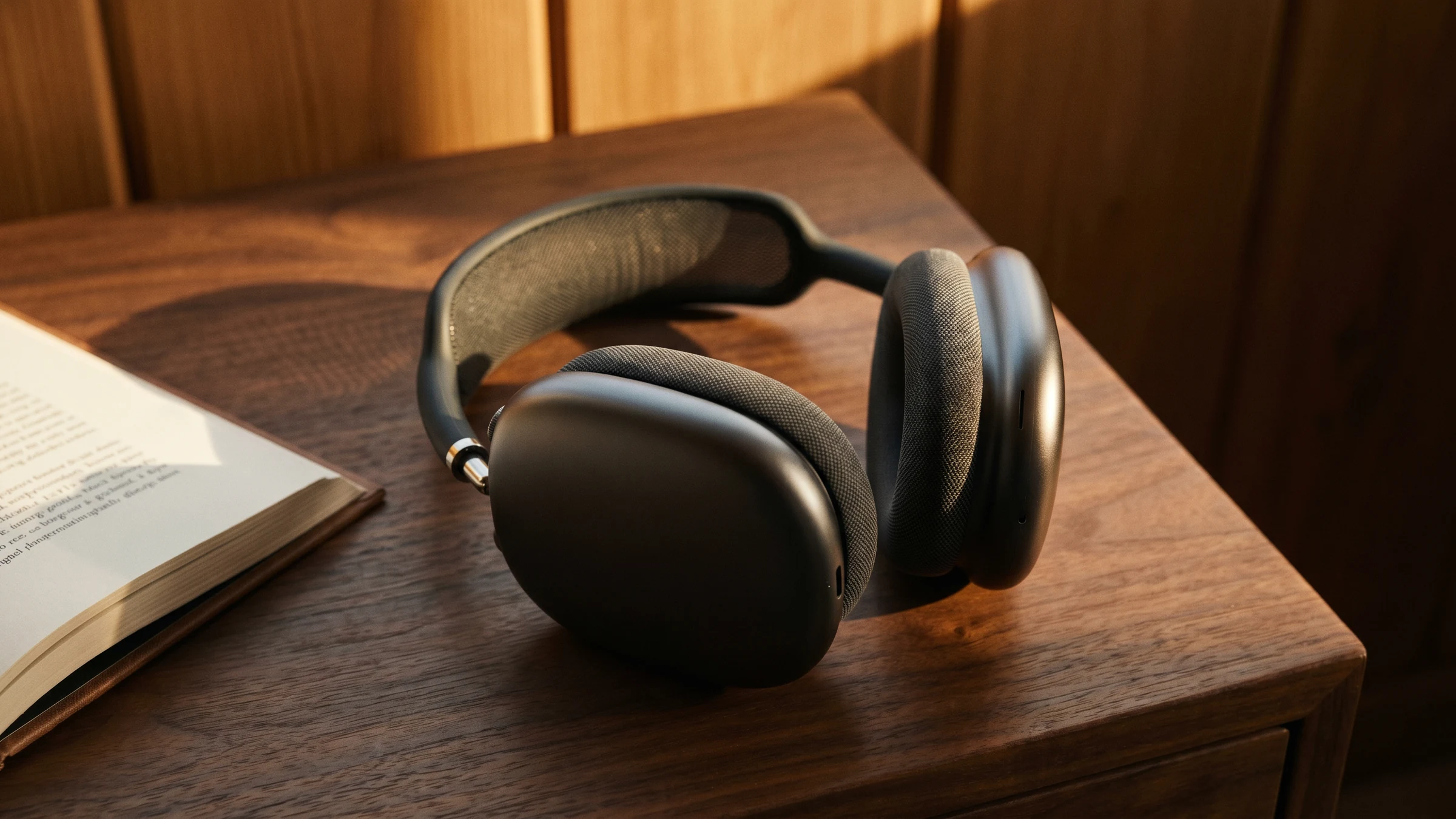 Apple AirPods Max, ein aufgeschlagenes Buch und ein Smartphone mit Hörbuch-Player auf einem Walnussholz-Schreibtisch — die intime Zuhör-Ecke