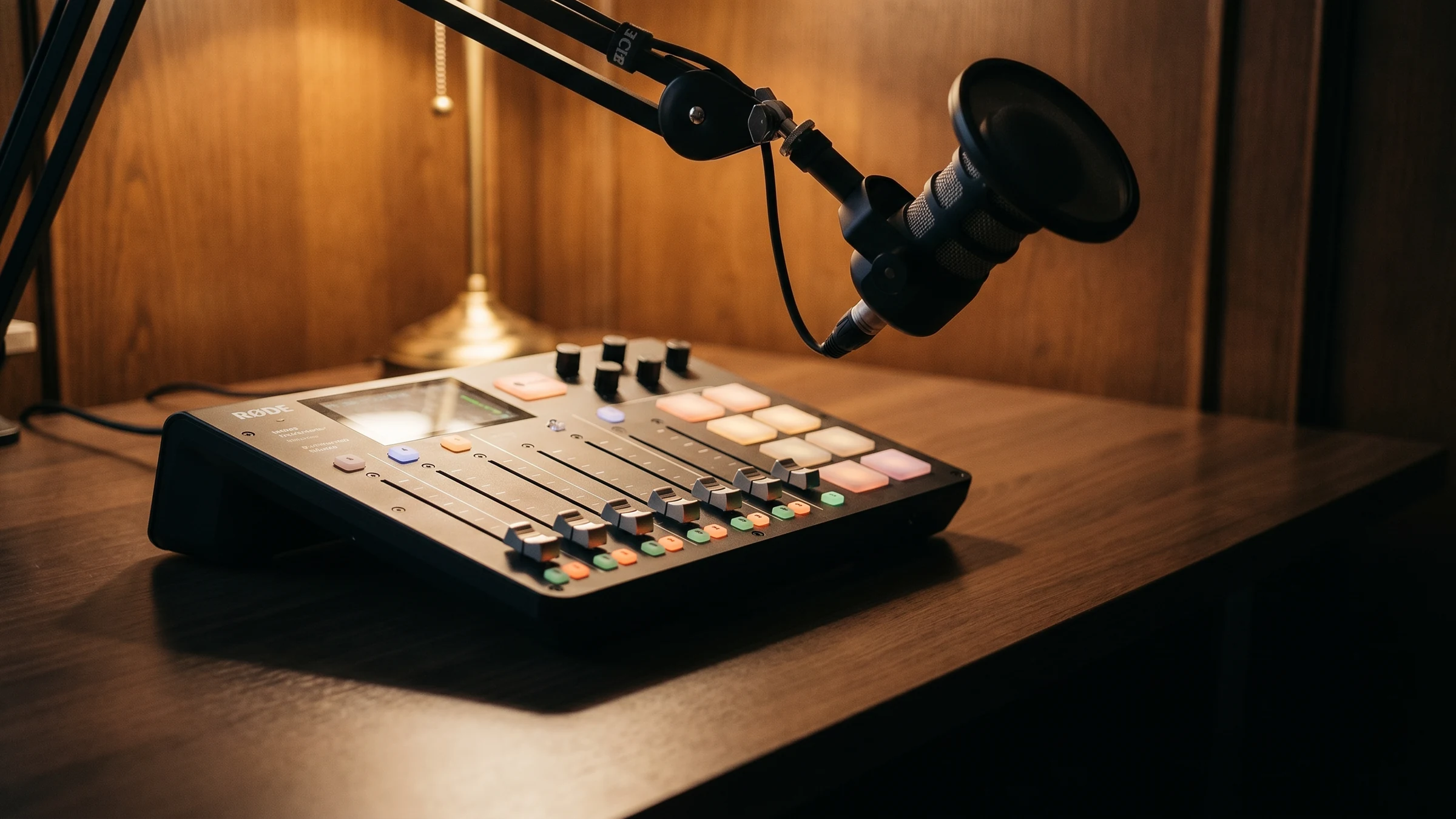Ein Schreibtisch mit Rodecaster-Duo-Konsole, Studio-Mikrofon und AirPods Max — der Aufnahmeplatz im Abendlicht