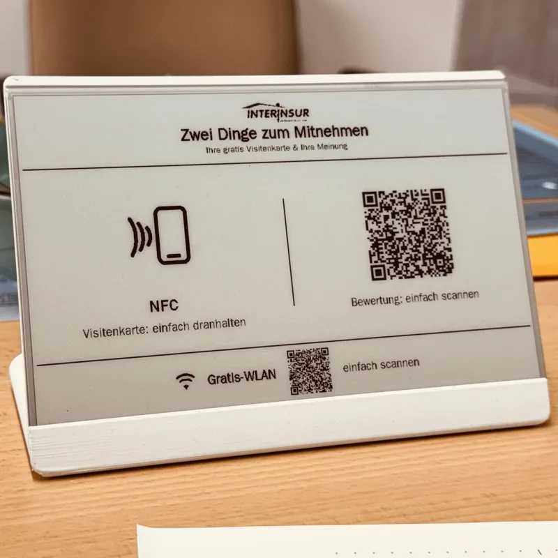 Ein weißes E-Paper-Display auf einer Theke mit NFC-Zeichen und zwei QR-Codes